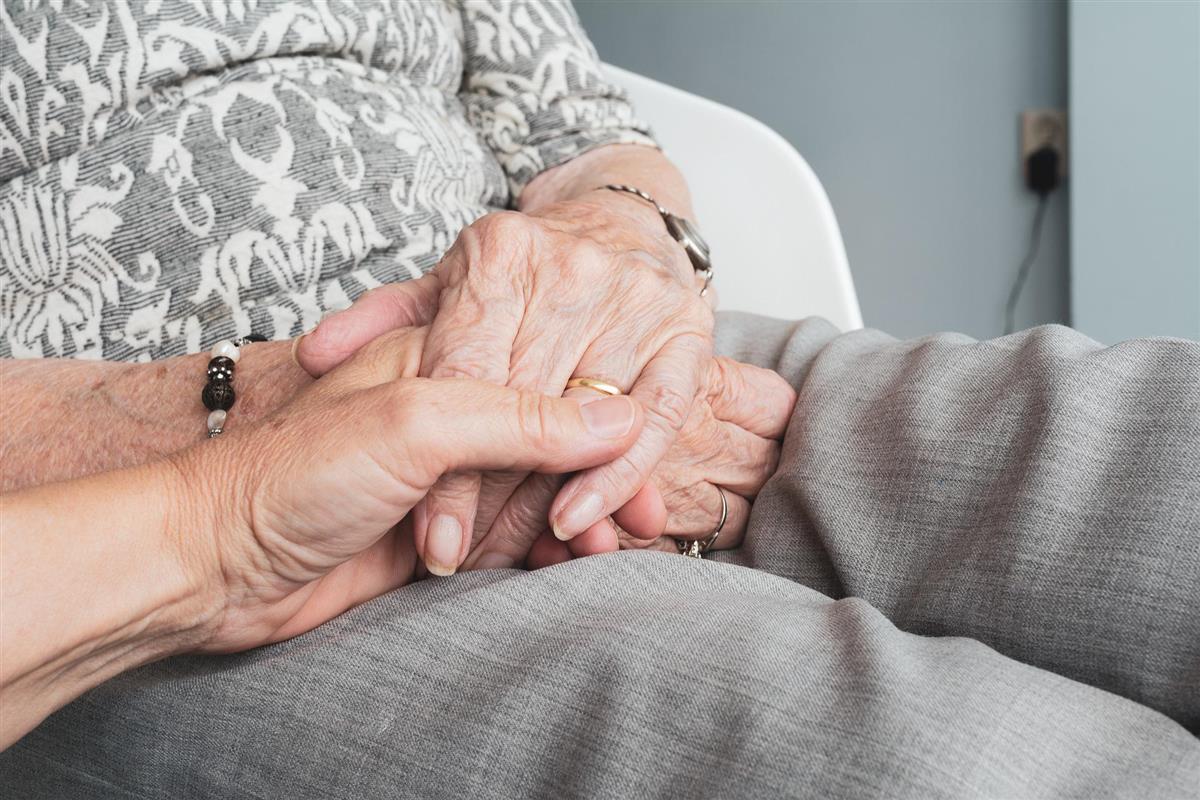 Ei eldre kvinne held i handa til ein yngre person. Kvinna har grå klede og bildet viser i hovudsak eit utsnitt av hendene. - Klikk for stort bilete