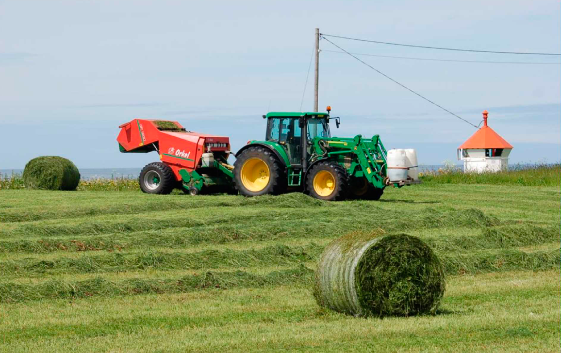 Bilde av grøn traktor som slår graset. Ein rundball i front. - Klikk for stort bilete