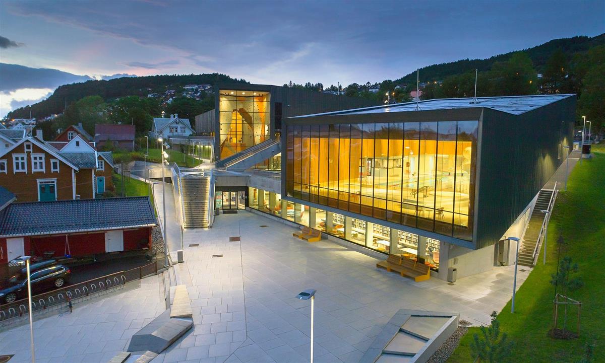 Bilde av Ulstein Arena i blåtimen – med lys i fleire store vindauge inn til symjebassenga. - Klikk for stort bilete
