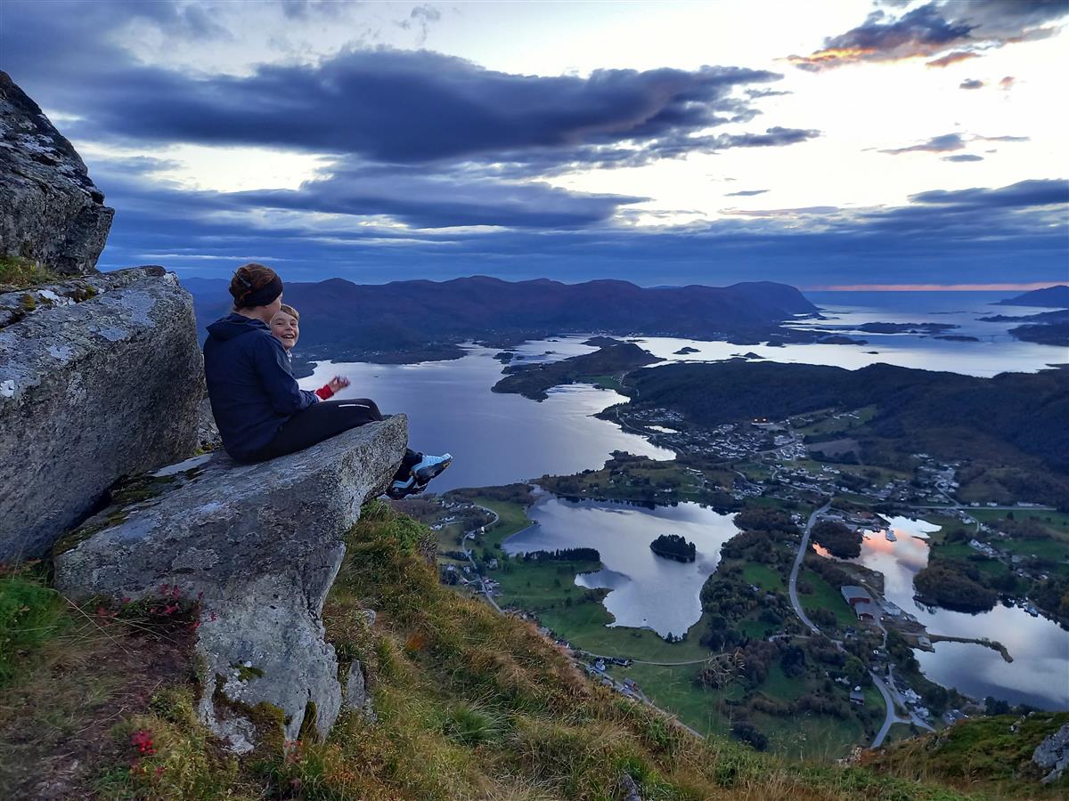To barn som sit på ei fjellhylle med utsikt mot Dimnøya. - Klikk for stort bilete
